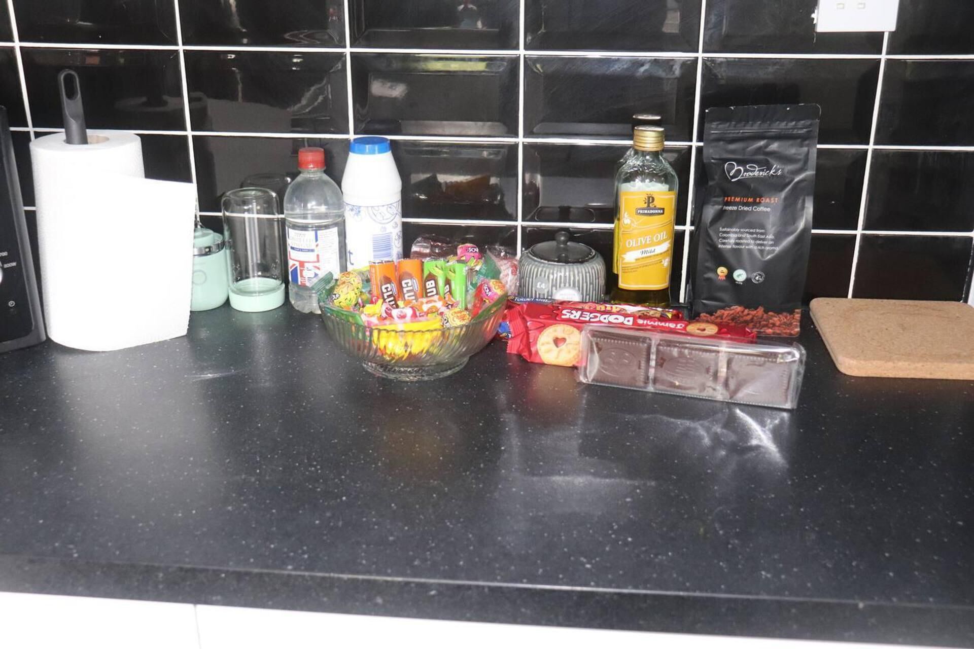 Un piano di lavoro in cucina con diversi oggetti, tra cui una bottiglia d'olio, una confezione di caffè, una ciotola di snack e una scatola di biscotti.