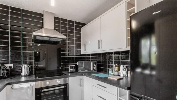 Cocina moderna con armarios negros y blancos, un refrigerador de acero inoxidable, un microondas, una tetera y un tostador.