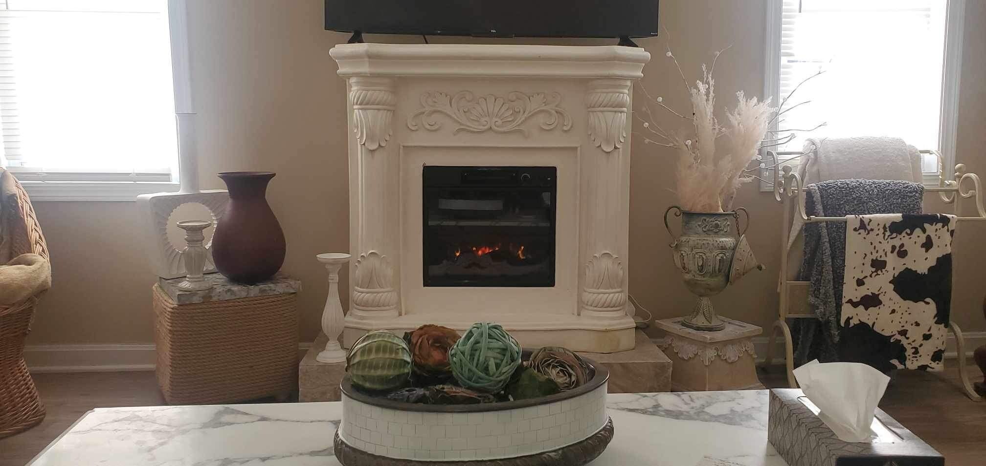 Un salon doté d’une cheminée, d’un téléviseur fixé au-dessus, et de divers objets décoratifs, notamment un vase, un panier et une table agrémentée d’un centre de table.