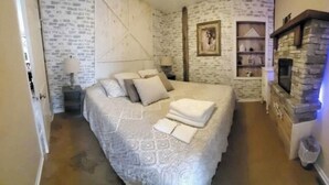 Un dormitorio con una cama, una mesita de noche, un estante en la pared y una chimenea de piedra.