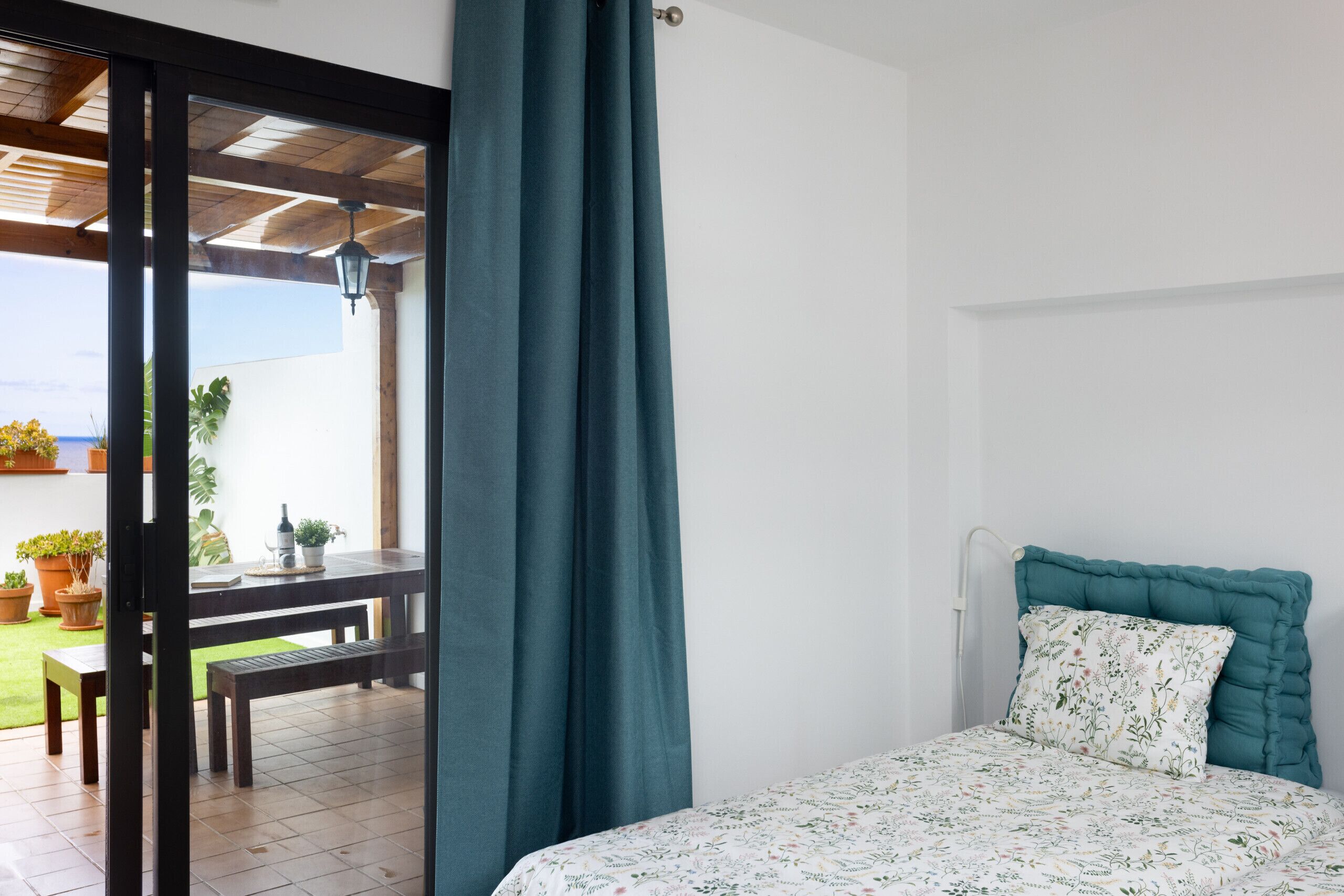 Un dormitorio con cama, una ventana con cortinas, vistas al exterior y una pequeña mesa con sillas.