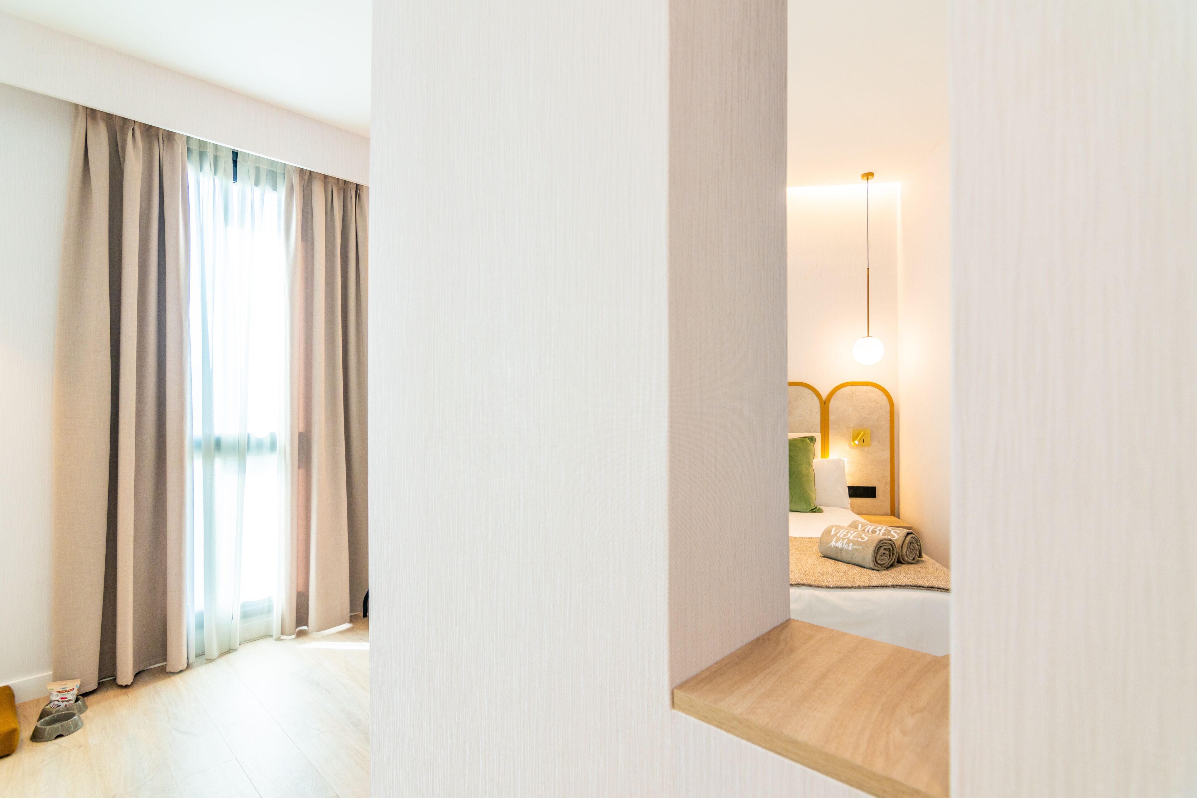 Hotellihuone, jossa on suuri ikkuna, puinen hylly ja yöpöytä, jossa on lamppu ja rullalle taitettu pyyhe.