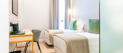 Una habitación de hotel con dos camas, un escritorio, una silla y una ventana con cortinas.