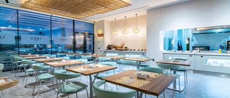 A modern restaurant with a high ceiling, exposed brick walls, and a mix of seating arrangements.