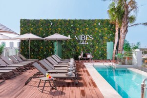A poolside area with lounge chairs and umbrellas, a green wall with plants, and a sign that reads "VIBES hotels".