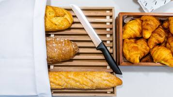 A wooden cutting board with a knife, a baguette, a croissant, and a box of croissants.