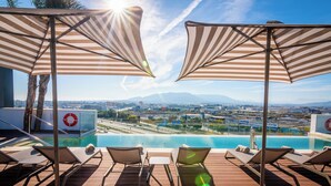A poolside area with lounge chairs and striped umbrellas, overlooking a cityscape and mountains. - Hotel Málaga Vibes (Málaga)