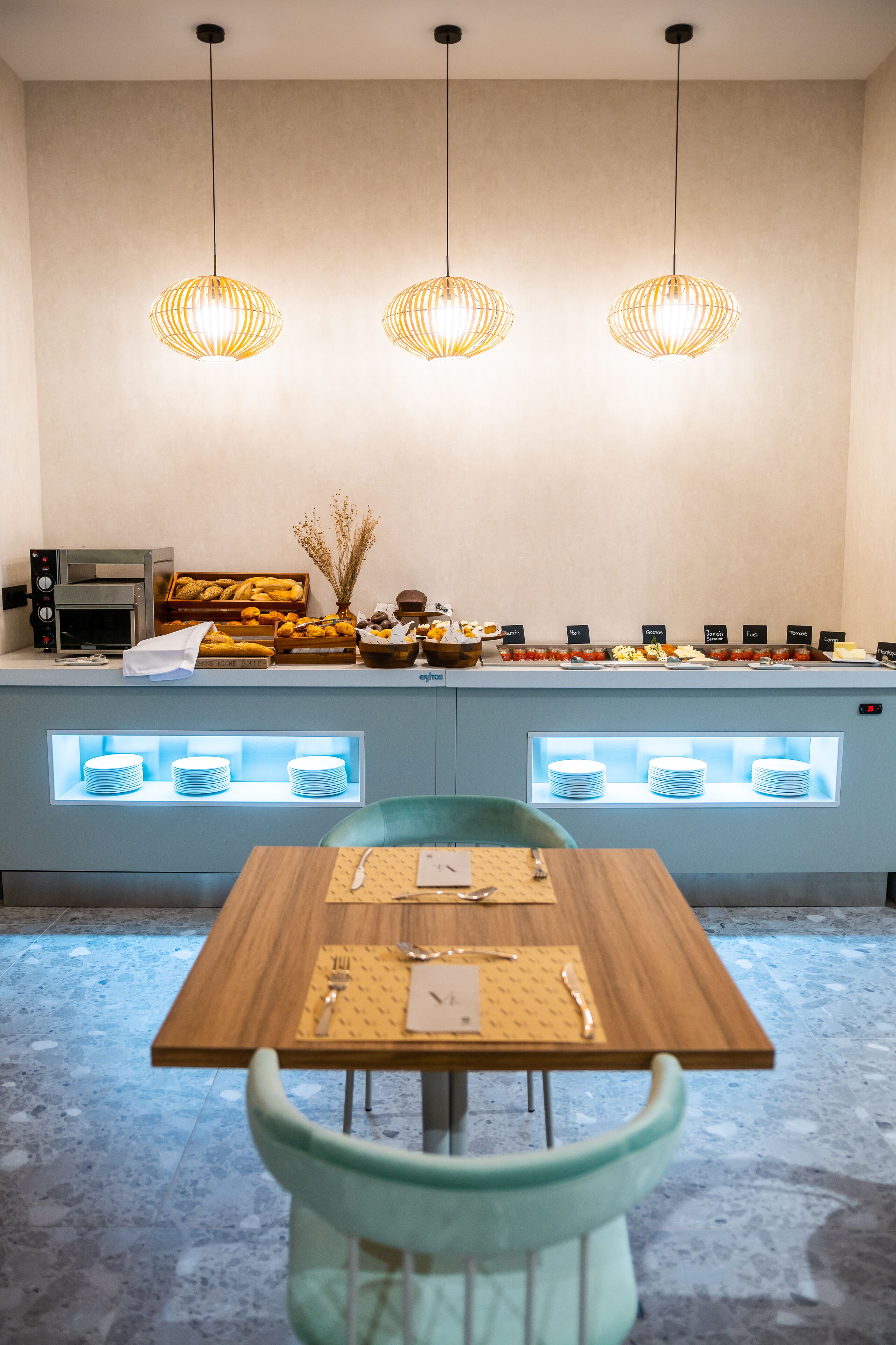 A breakfast buffet area with a wooden table, chairs, and a counter displaying various food items.