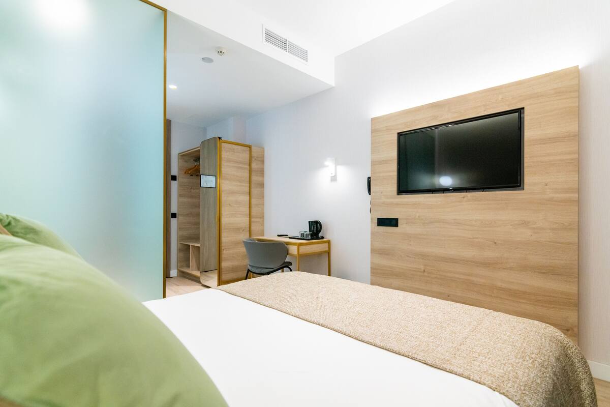 A modern hotel room with a bed, a desk, a chair, and a TV mounted on the wall.