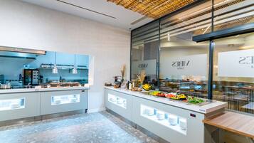 A modern kitchen with a buffet area, featuring a glass partition and a variety of food items displayed on the counter.