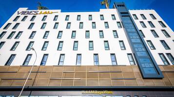 Un bâtiment d’hôtel moderne, sur lequel on peut lire les inscriptions « VIBES hotels » et « Hotel Málaga Vibes ».