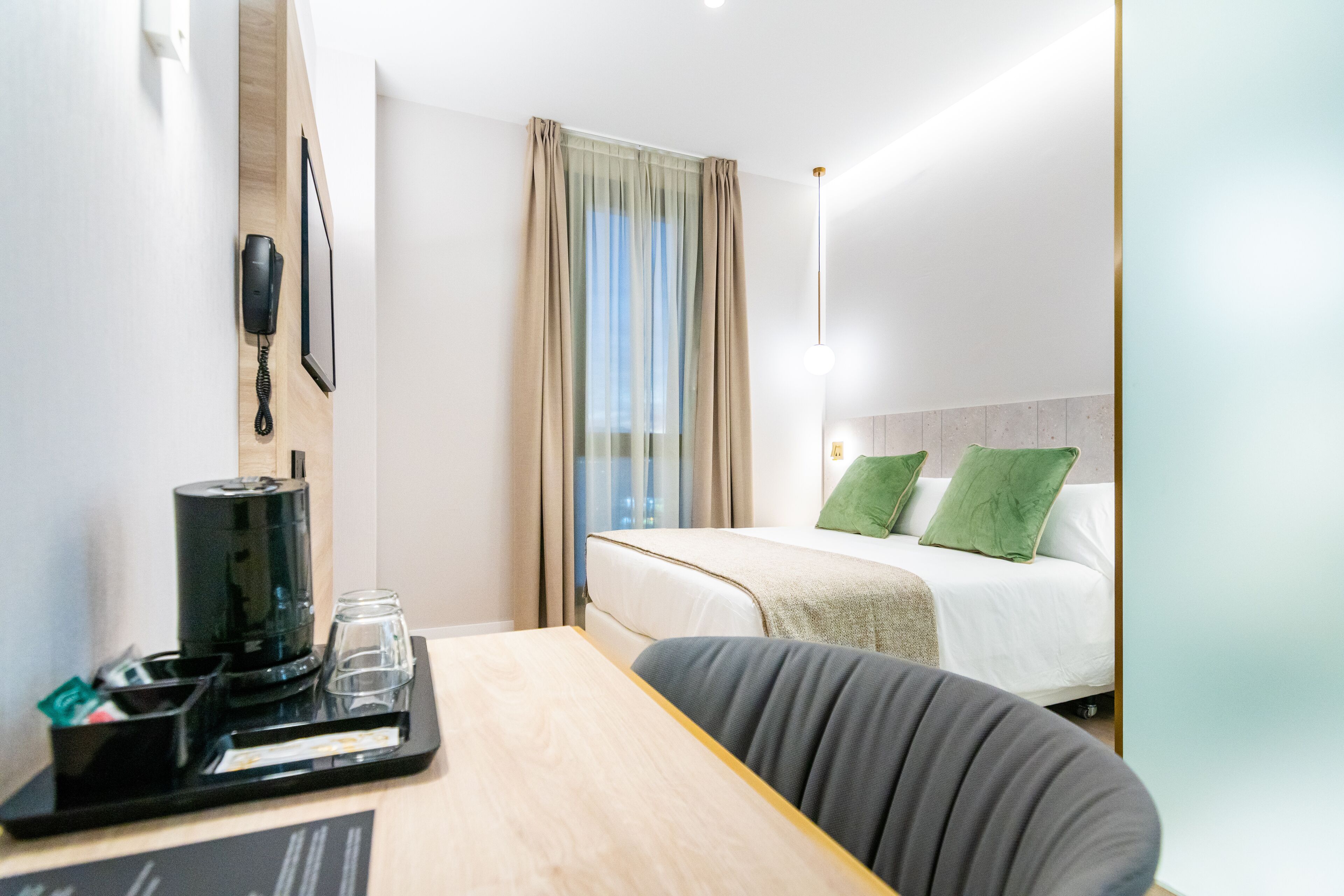 Une chambre d’hôtel avec un lit, un bureau doté d’une machine à café, un téléphone et une fenêtre avec des rideaux.