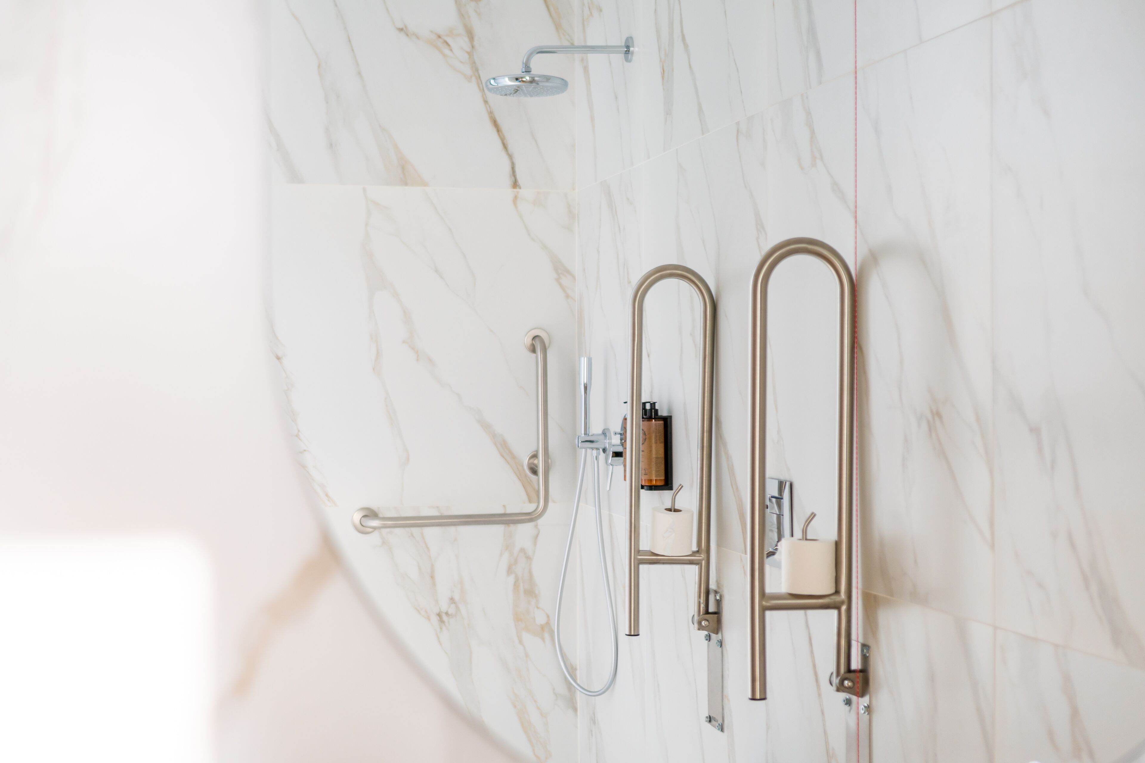 A bathroom with a marble floor, a shower with a handheld showerhead, and a toilet with a paper towel holder.