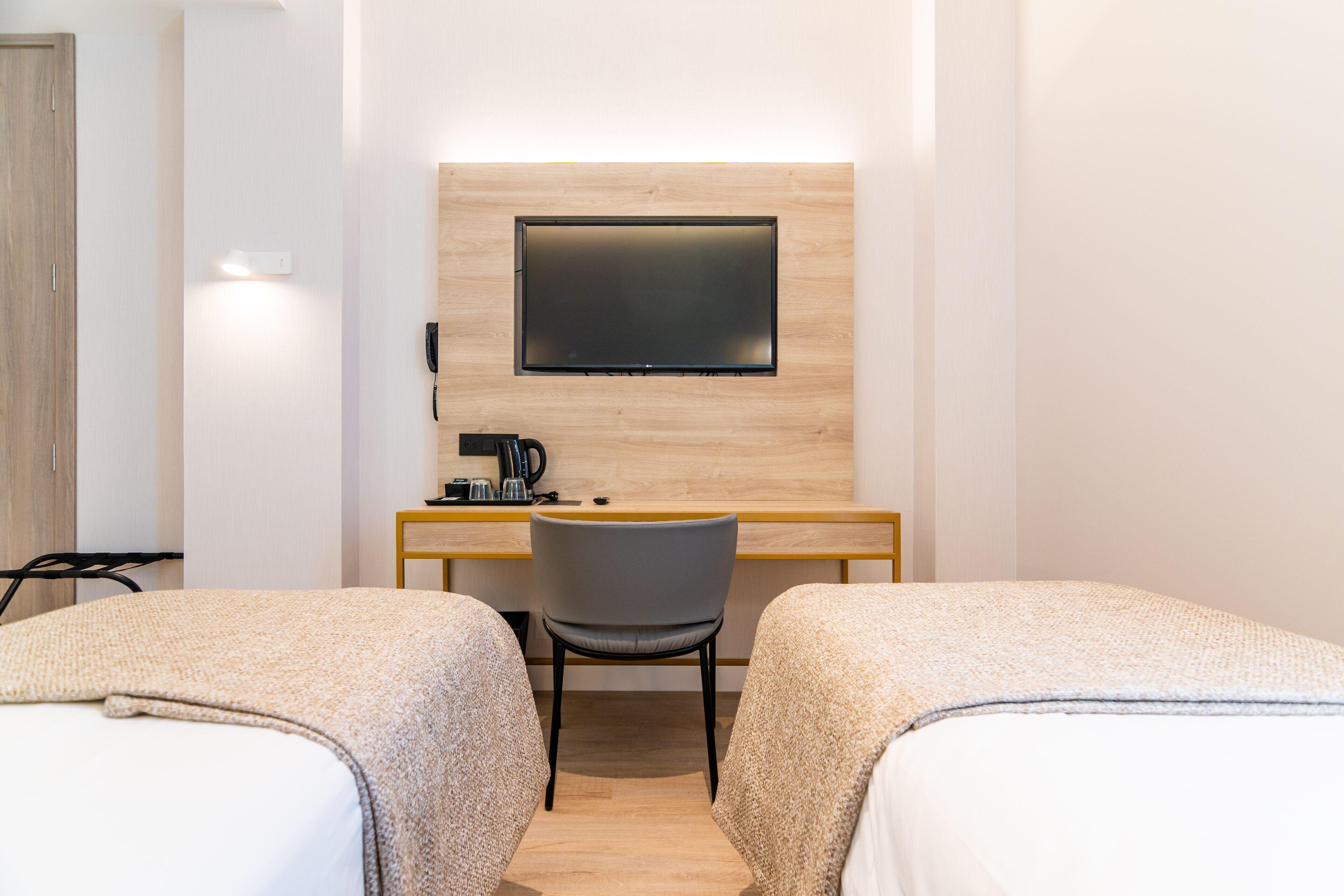 A hotel room with two beds, a desk, a chair, a flat-screen TV mounted on the wall, and a telephone.