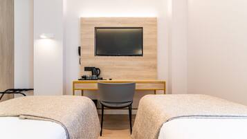 A hotel room with two beds, a desk, a chair, a flat-screen TV mounted on the wall, and a telephone.