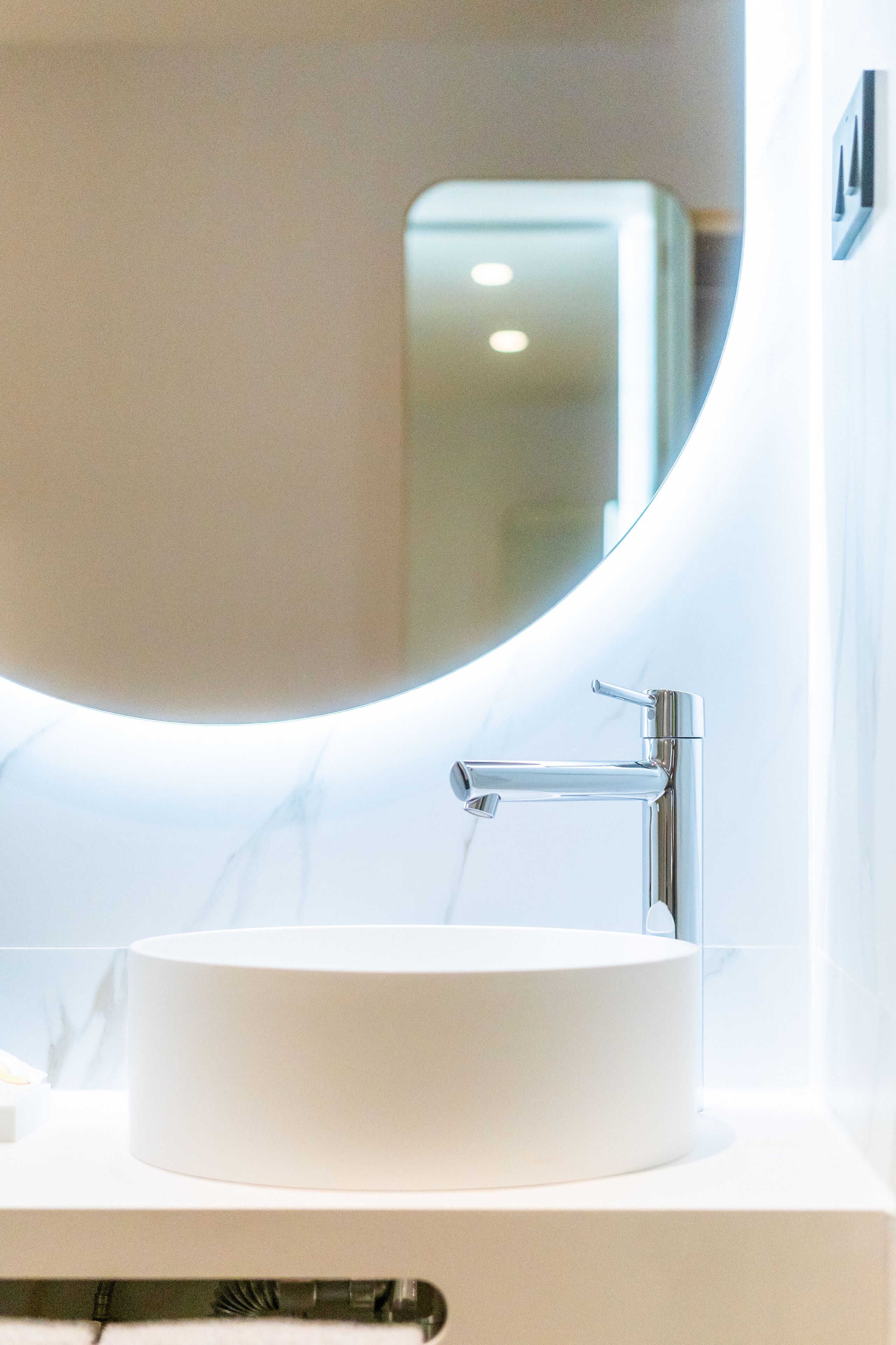 Un baño moderno con un espejo redondo, un grifo cromado y un lavabo blanco.