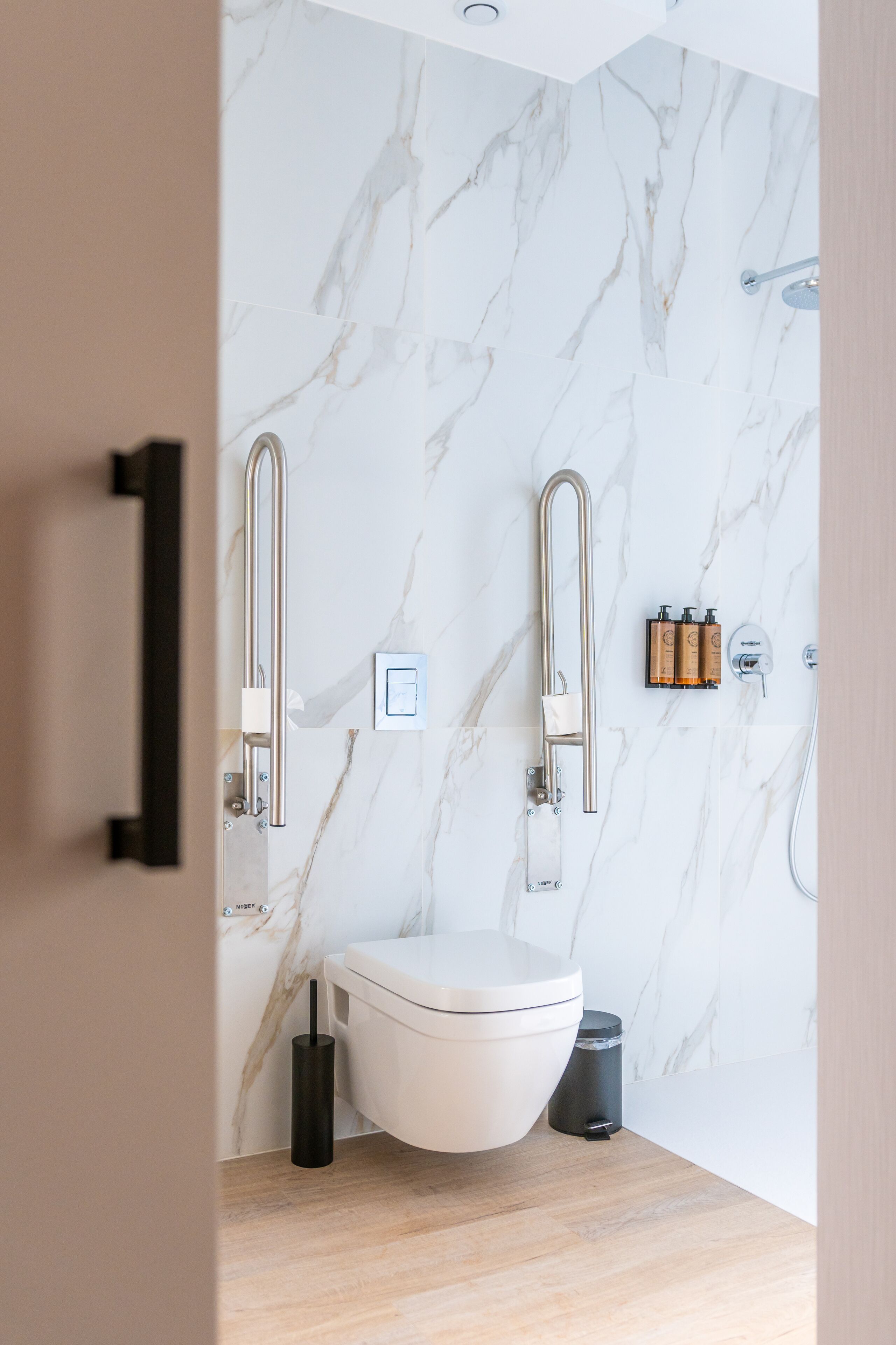 A modern bathroom with a marble backsplash, a toilet, a bidet, and a trash can.