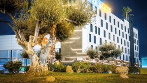 A modern hotel with a prominent "VIBE'S Hotels" sign, surrounded by landscaped greenery and palm trees. - Hotel Málaga Vibes (Málaga)