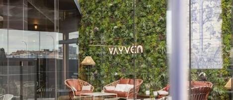 A modern interior with a glass wall, a green vertical garden, and seating areas with white and brown chairs.