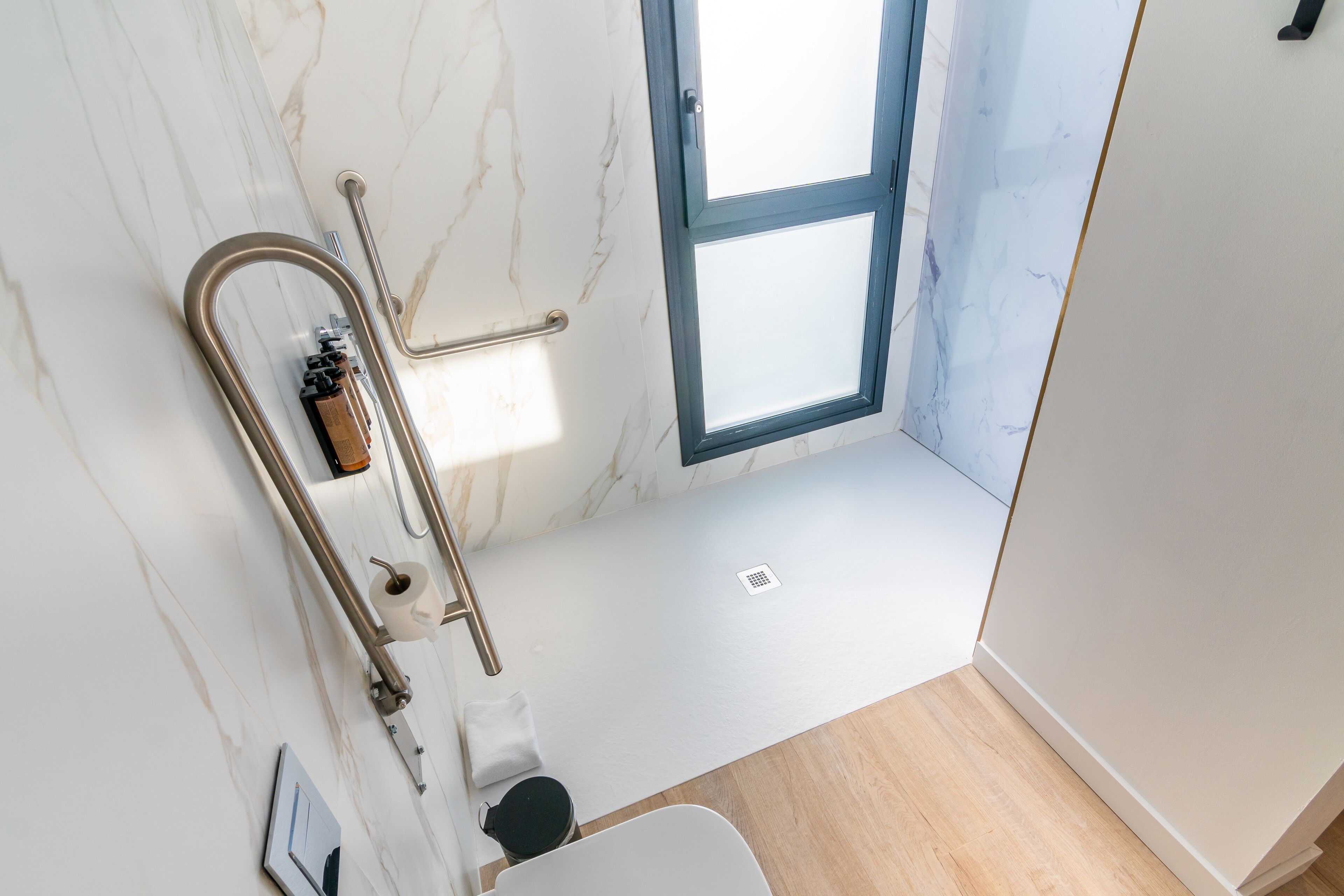 Un baño con pared de mármol, una ventana, un inodoro y zona de ducha.