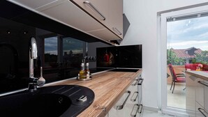 Una cocina moderna con una isla grande, horno empotrado y vistas a un balcón con mobiliario exterior.