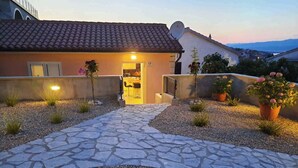 Una casa con un sendero de piedra que lleva a una puerta amarilla, rodeada de grava y macetas con plantas.