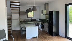 A modern kitchen with a central island, a built-in oven, a black refrigerator, and a window providing natural light. - Jolie Maison en Bois, Tout Confort, Proche Océan (Vielle-Saint-Girons)