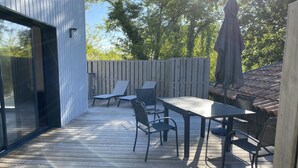 A wooden deck with a table and chairs, a glass door, and a wooden fence. - Jolie Maison en Bois, Tout Confort, Proche Océan (Vielle-Saint-Girons)