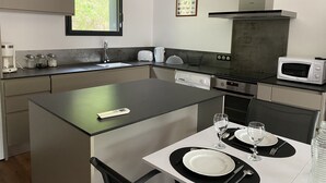 A modern kitchen with a central island, a built-in dishwasher, a microwave, and a window overlooking greenery. - Jolie Maison en Bois, Tout Confort, Proche Océan (Vielle-Saint-Girons)