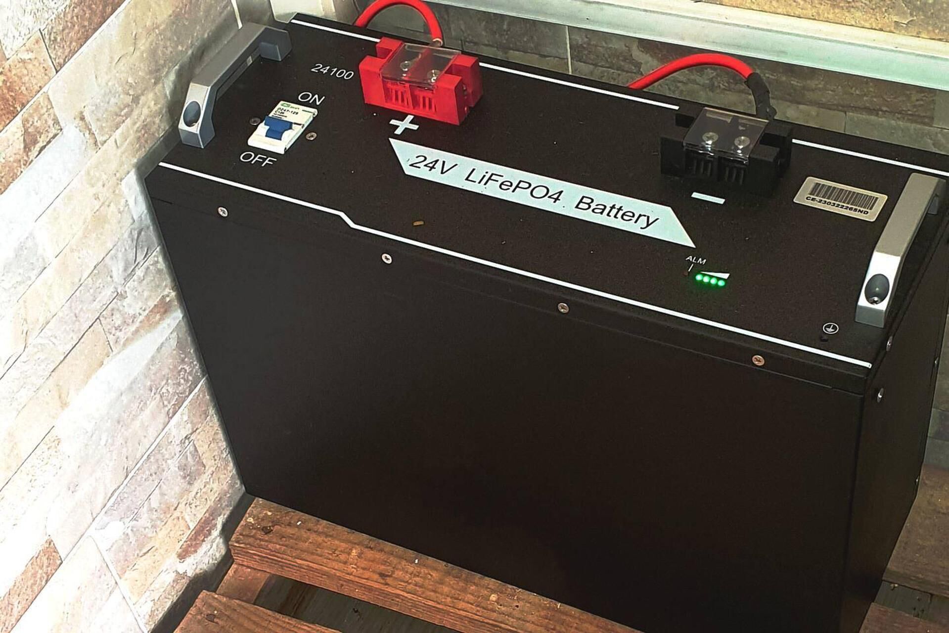 Et 24V LiFePO4 batteri med etiket, et rødt og sort kabel og en kontakt.