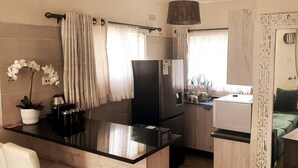 A compact kitchen with a black refrigerator, a coffee machine, and a small dining area with a white chair. - Gorgeous 1-bed Apartment in Harare (Harare)