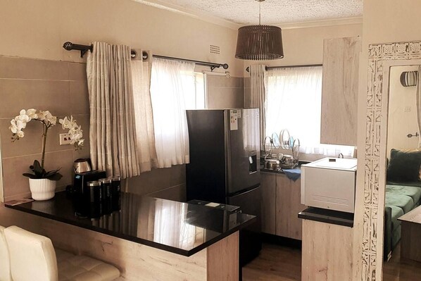 A compact kitchen with a black refrigerator, a coffee machine, and a small dining area with a white chair.
