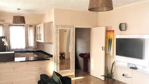 A modern living room with a sofa, a TV, and a kitchen area with a sink and cabinets. - Gorgeous 1-bed Apartment in Harare (Harare)