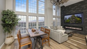 A spacious living room with a large window, a fireplace, a dining area, and a ceiling fan. - New Luxury Prescott Lynx B B 4k ft2 Sleeps 22 (Prescott)