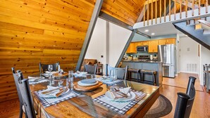 A dining area with a wooden table set for four, a kitchen in the background, and a staircase leading to an upper level. - Spacious A-frame Pines Cabin 12 Beds Loft Game Room (Flagstaff)