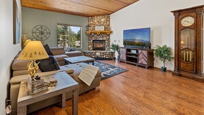 A cozy living room with a stone fireplace, a large flat-screen TV, and a wooden ceiling fan. - Spacious A-frame Pines Cabin 12 Beds Loft Game Room (Flagstaff)