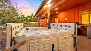 A hot tub with a stone exterior, a wooden deck, and a view of a building with a red exterior and a window. - Spacious Canyon Peak Pine View Home Game Room Hot Tub (Flagstaff)