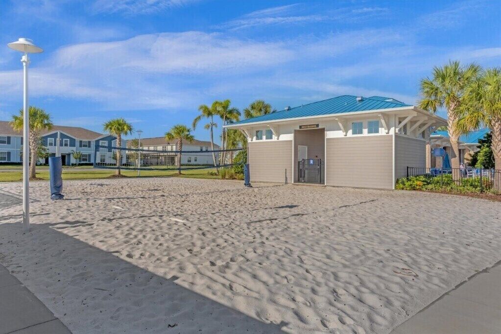 Un hotel frente a la playa con zona de piscina techada, una red de voleibol y palmeras al fondo.