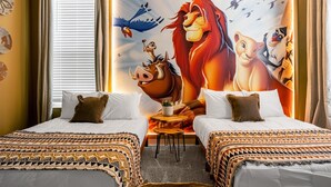 Ein Hotelzimmer mit zwei Betten, einer großen Wandmalerei von Zeichentrickfiguren, einem Fenster mit Vorhängen und einem kleinen Tisch mit einer Pflanze.