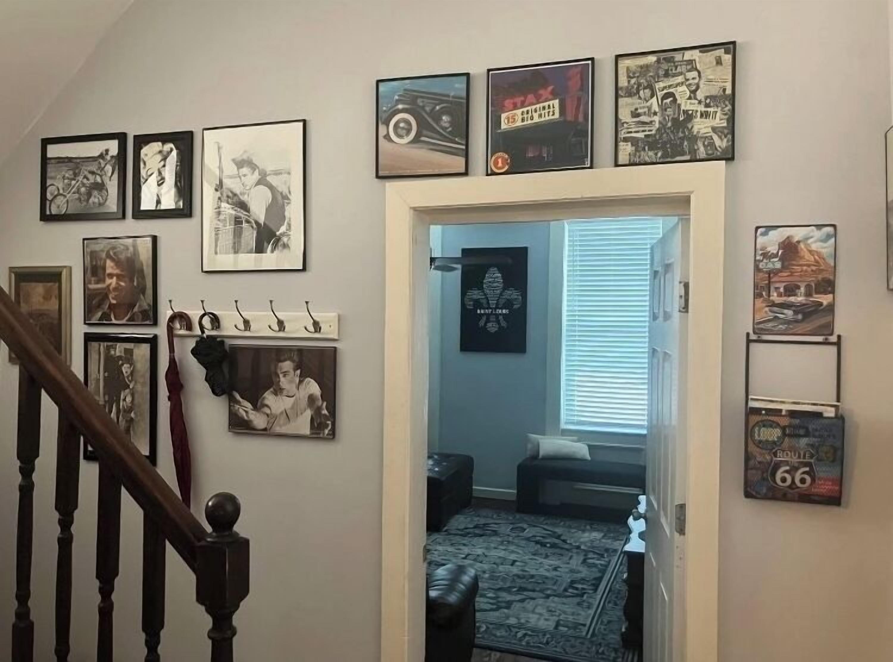A hallway with framed pictures on the walls, a staircase, and a rug leading to a room.