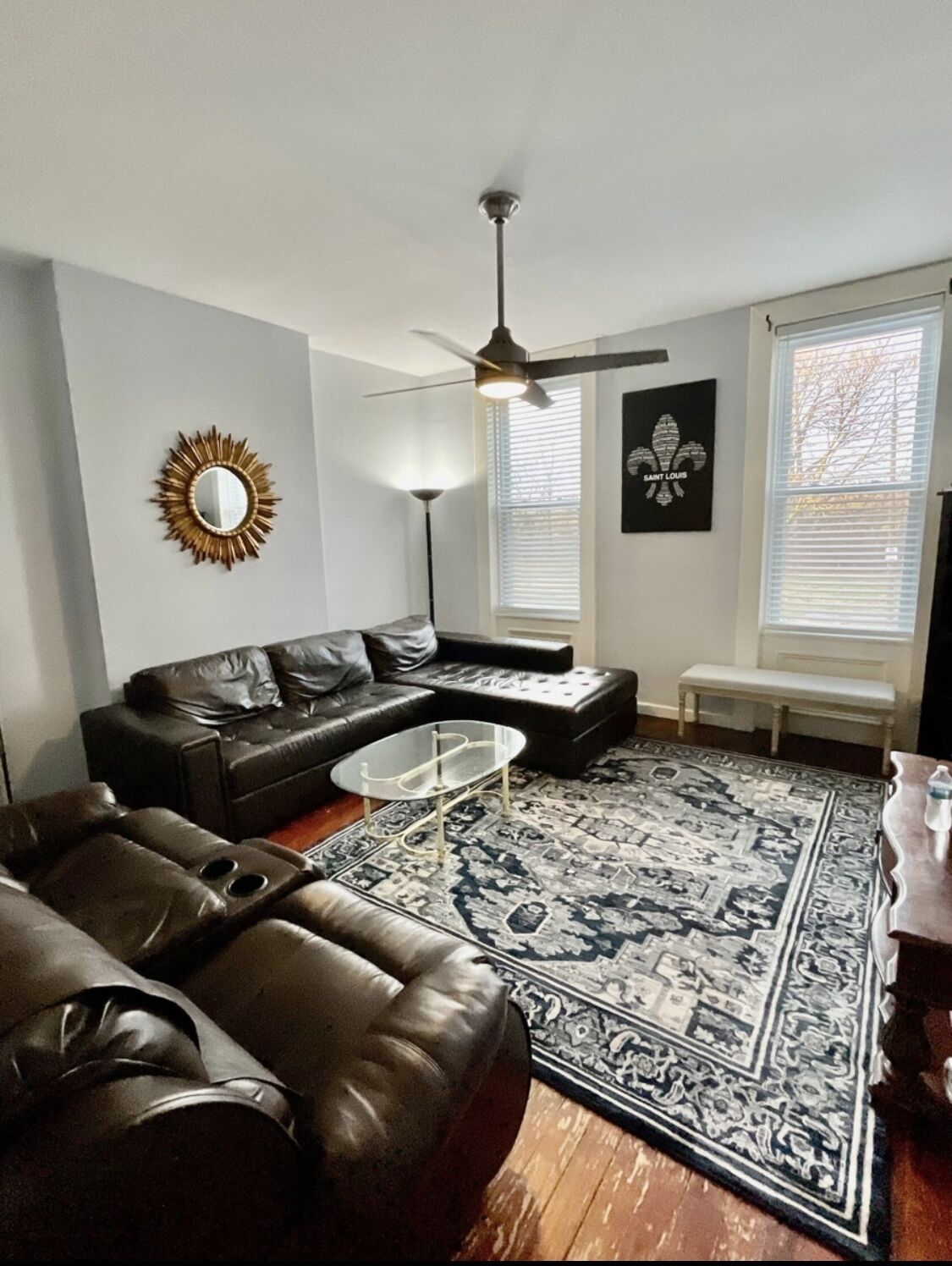 A living room with a sectional sofa, a coffee table, a patterned rug, a ceiling fan, and a wall-mounted mirror.