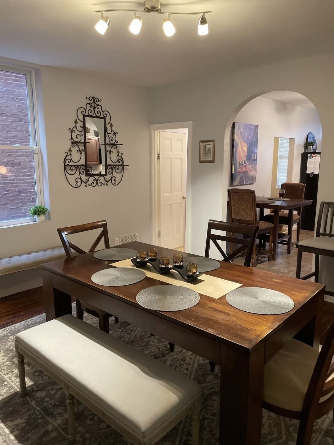 A dining area with a wooden table, four chairs, a bench, and a decorative mirror on the wall.