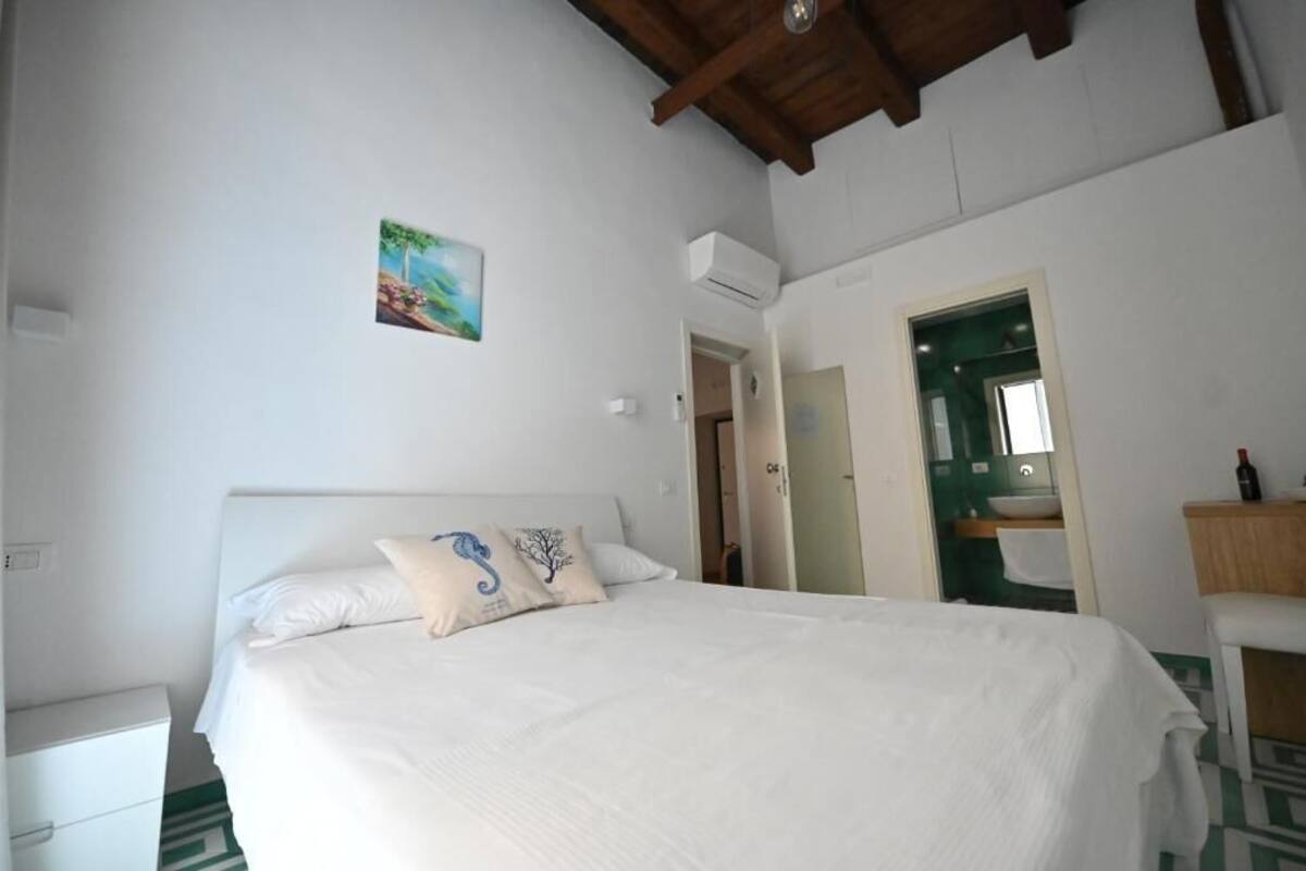 A bedroom with a large bed, a small bedside table, a painting on the wall, and an open door leading to a bathroom.