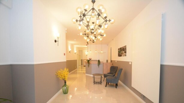 A hotel lobby with a chandelier, a reception desk, a seating area, and a vase of flowers.