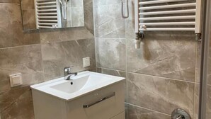 Un baño con tocador blanco, un espejo, toallero y una ducha con puerta de cristal.