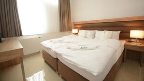 A hotel room with a large bed, two bedside tables, a wooden headboard, and a window with curtains.
