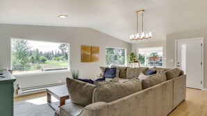 A modern living room with a sectional sofa, large windows, and a view of a park. - Chehalis Getaway w/ Golf Course View + Fire Pit! (Chehalis)