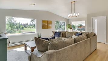 A modern living room with a sectional sofa, large windows, and a view of a park.