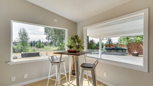 A room with two large windows, a wooden table with a plant, and two white bar stools. - Chehalis Getaway w/ Golf Course View + Fire Pit! (Chehalis)