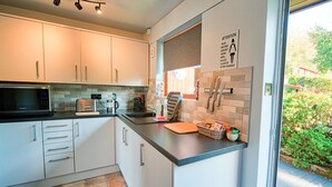 A modern kitchen with white cabinets, a microwave, toaster, and a sink. There is a sign on the wall and a window with a view of greenery outside. - Arenig - Bala Lake (Bala)